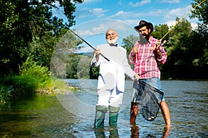 Two men friends fisherman fishing on river. Old father and son with rod fishing at riverside. Recreational activity.