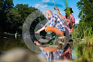 Two men friends fisherman fishing on river. Old father and son with rod fishing at riverside. Recreational activity.