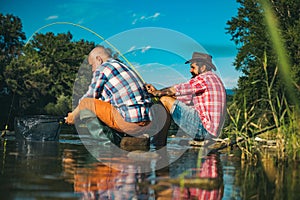 Two men friends fisherman fishing on river. Old father and son with rod fishing at riverside. Recreational activity.