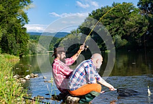 Two men friends fisherman fishing on river. Old father and son with rod fishing at riverside. Recreational activity.