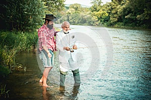 Two men friends fisherman fishing on river. Old father and son with rod fishing at riverside. Recreational activity.