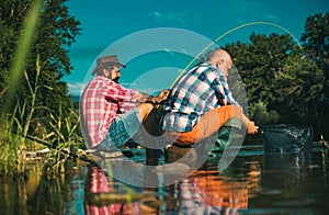 Two men friends fisherman fishing on river. Old father and son with rod fishing at riverside. Recreational activity.