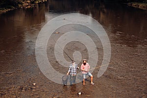Two men friends fishing. Flyfishing angler makes cast, standing in river water. Old and young fisherman.