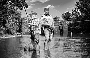 Two men friends fishing. Flyfishing angler makes cast, standing in river water. Old and young fisherman.