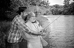 Two men friends fishing. Flyfishing angler makes cast, standing in river water. Old and young fisherman.