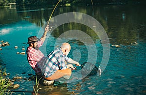 Two men friends fishing. Flyfishing angler makes cast, standing in river water. Old and young fisherman. Catching trout