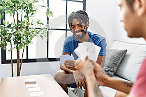 Two men friends playing poker cards sitting on sofa at home