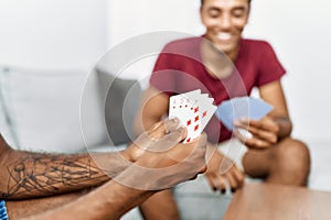 Two men friends playing poker cards sitting on sofa at home