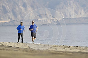 Two men friends running together on beach sand coast mountain bachground in healthy lifestyle concept