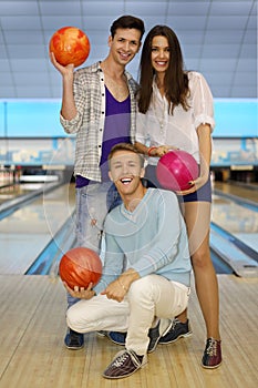 Two men and girl hold balls in bowling club