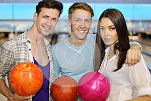 Two men and girl hold balls in bowling club