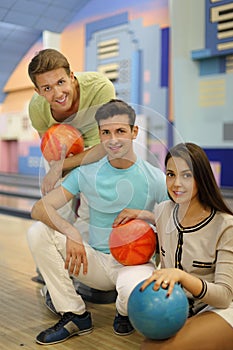 Two men and girl hold balls in bowling club