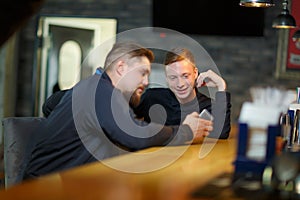 Two men, have an conversation, contemplating a modern smartphone sitting in a bar.