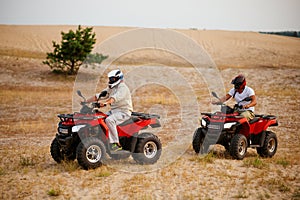 Two men in helmets, atv riding in desert sands