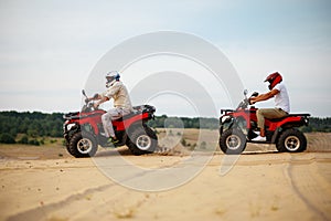 Two men in helmets, atv riding in desert sands