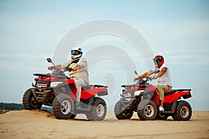 Two men in helmets, atv riding in desert sands