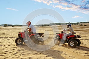 Two men in helmets ride on atv in desert