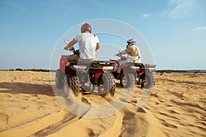 Two men in helmets riding on atv in desert sands