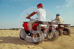 Two men in helmets riding on atv in desert sands