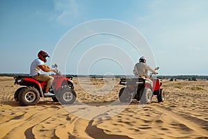 Two men in helmets riding on atv in desert sands