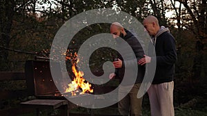 Two men in jackets are burning a bonfire in the evening in the autumn forest.