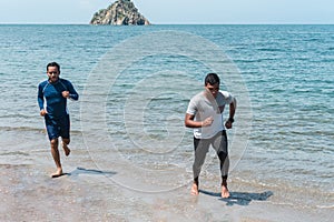 Two men jogging on the beach. Male runners training outside exercising