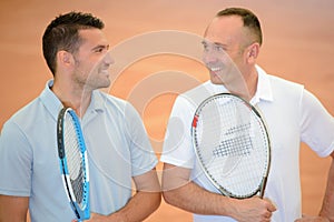 Two men joking together holding tennis rackets