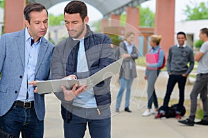 two men looking at folder while students wait in background