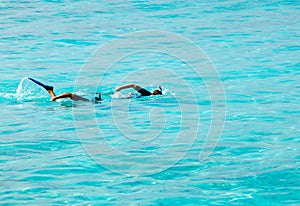 Two men with masks and tubes swim synchronously