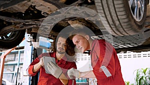 two men are mechanics, working in large garage, two mechanics checking undercarriage car raised high see lower part clearly,