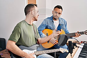 Two men musicians playing classical and electrical guitar looking smartphone screen at music studio