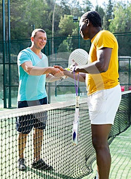 Two men padel tennis players shake hands amicably