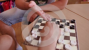 Two men play checkers on the edge of a wooden table. Close-up of the Board with checkers and men`s hands.