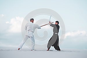 Two men practicing Japanese martial arts in desert