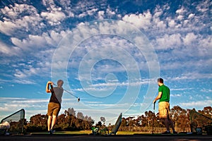 Two men practicing their golf swing at a driving range