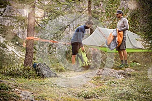 Two men preparing hanging tent camping near forest woods.Group of friends people summer adventure journey in mountain