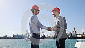 Two men in protective orange helmets greet each other by shaking hands.