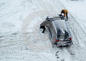 Two men push out a car stuck in the snow. The car skids in a snowdrift on an icy road. Uncleaned roads from snow. Copy space for