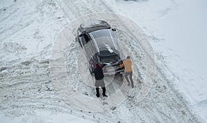 Two men push out a car stuck in the snow. The car skids in a snowdrift on an icy road. Uncleaned roads from snow. Copy space for