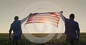 Two men raise up the US flag against the backdrop of a wheat field at sunset