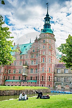 Two men are resting on the grass nearby Frederiksborg slot Castle near Copenhagen. Hillerod, Denmark. Exotic amazing places.