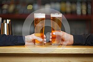 Two men`s hands hold two glasses with a beer.