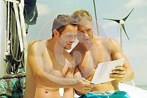 Two men on a sail boat looking at the screen of a tablet