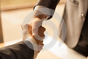 Two men shaking hands over sunny office background. Partnership