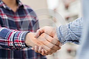 Two men shaking hands to dealing success agreement business. Business people wearing scott shirt on city view background