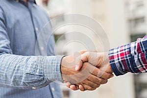 Two men shaking hands to dealing success agreement business. Business people wearing scott shirt on city view background