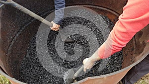 two men with shovel removing charcoal in a drum. use of biochar in the vegetable garden and preparing it