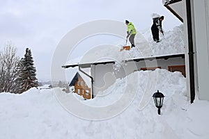 Two men shoveling high, heavy snow from a house roof