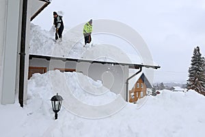 Two men shoveling high heavy snow from a house roof