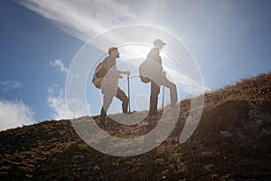 Two men silhouettes walking along the top of the mountain